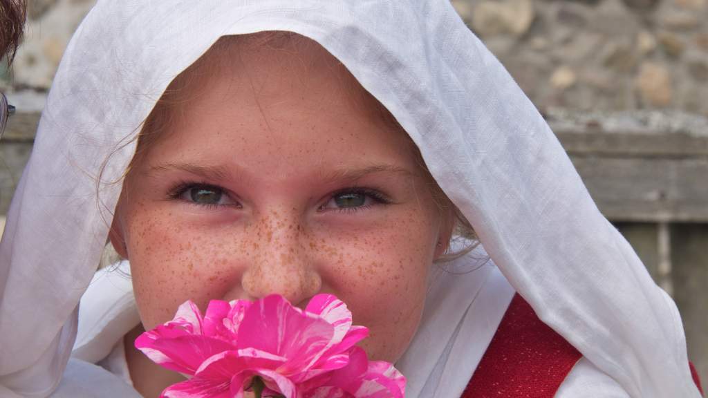 Young reenactor girl smelling a bright flower at the Fortress of Louisbourg, Cape Breton Island, Nova Scotia